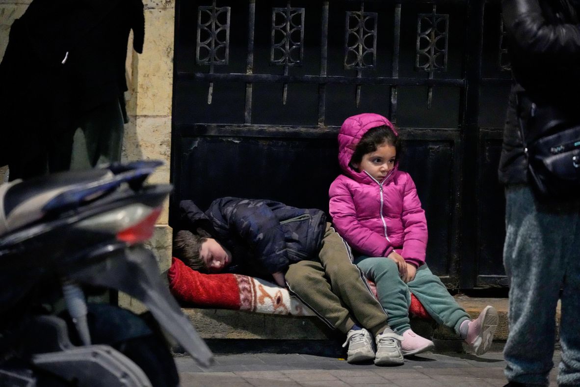 Children sit on a sidewalk as displaced families fleeing Israeli strikes arrive in the southern port city of Sidon, Lebanon, on Monday.