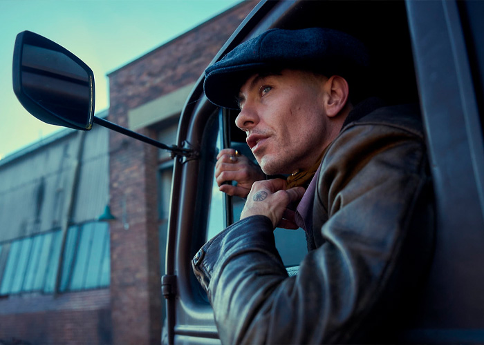 Barry Keoghan wearing a black cap and leather jacket, looking out from a vehicle against an urban background Barry Keoghan wearing a black cap and leather jacket, looking out from a vehicle against an urban background