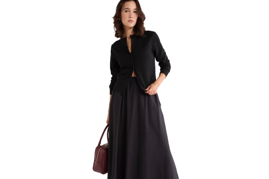 A woman wearing a black cardigan and a black maxi skirt.