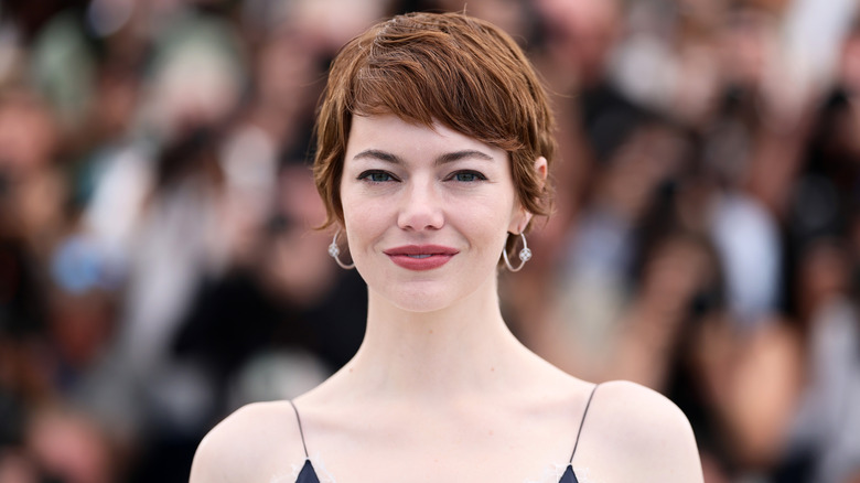 Emma Stone smiling in front of cameras in 2025