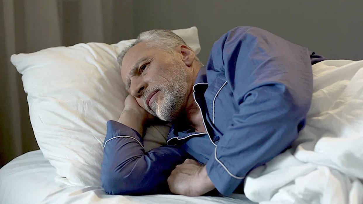 Man on side in bed, awake, suggesting sleep struggles.