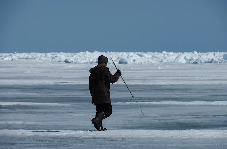 A seal hunter holds a spear on the ice