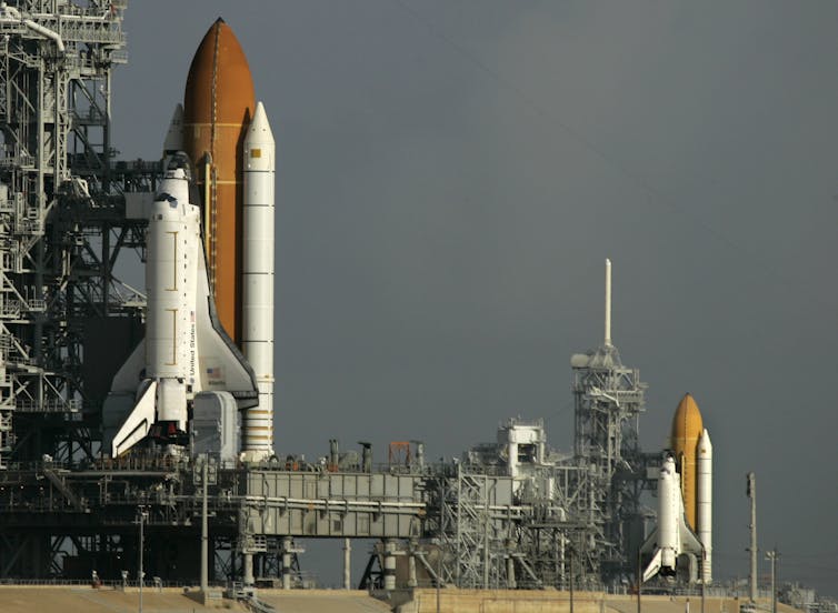 Two large spacecraft sitting on launchpads.