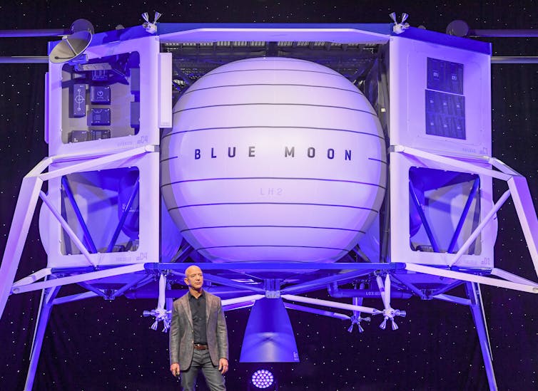Jeff Bezos stands in front of a large spacecraft lander labeled 'Blue Moon'