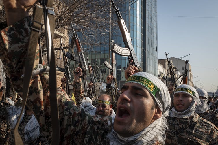 Military men holding rifles march on a street.