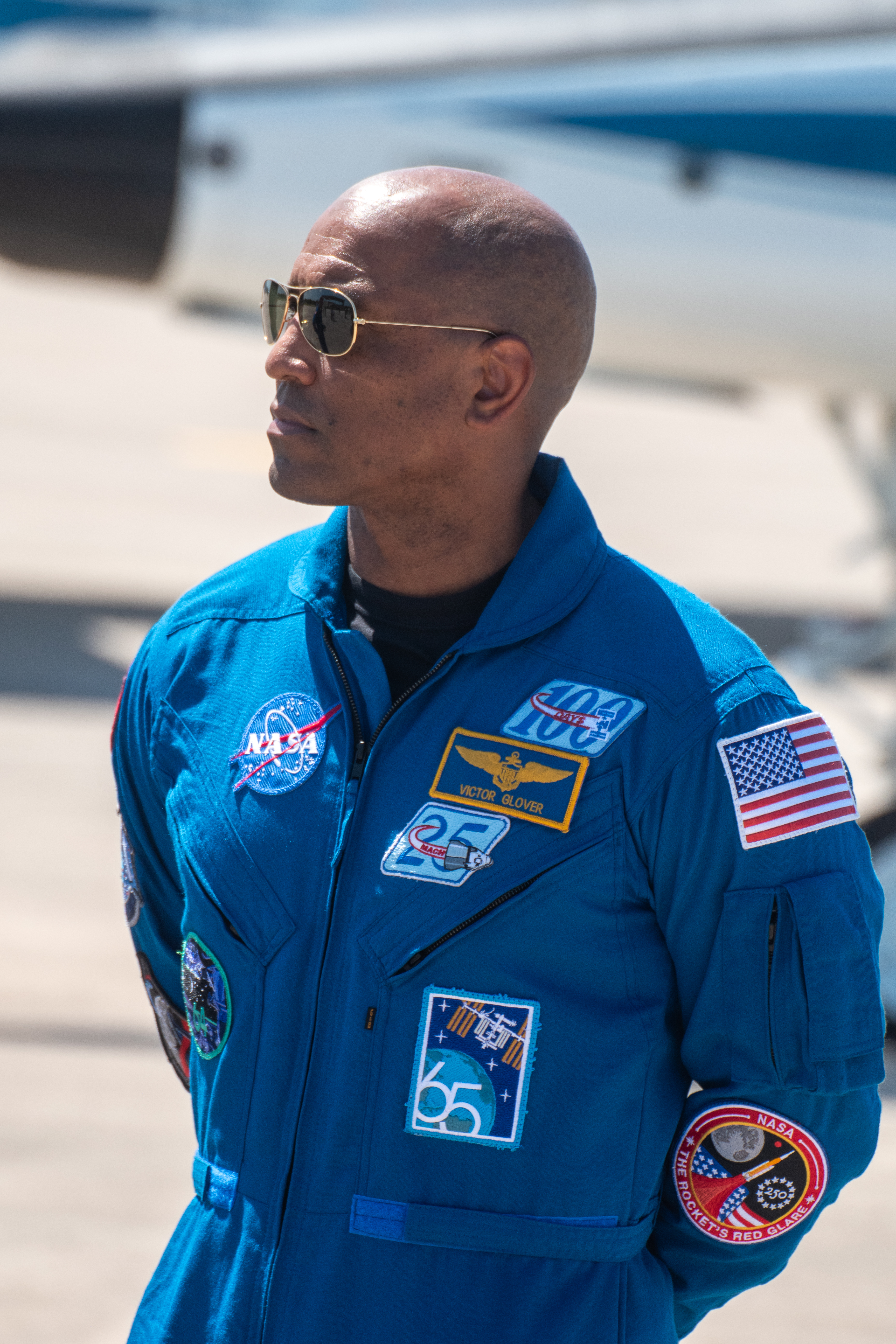 An astronaut in blue jumpsuit stands outside.