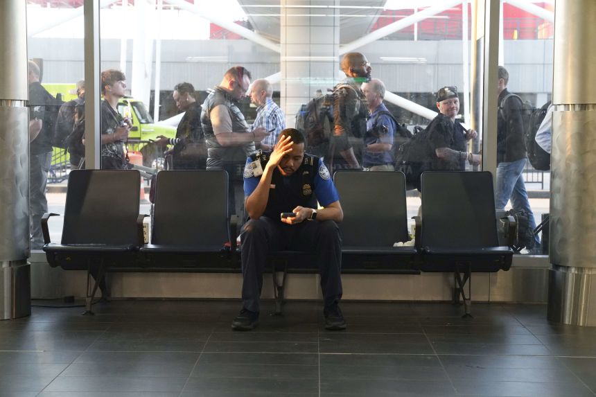 A TSA officer rests at Hartsfield-Jackson Atlanta International Airport on Monday as the passenger security line winds up and down the sidewalk behind him.
