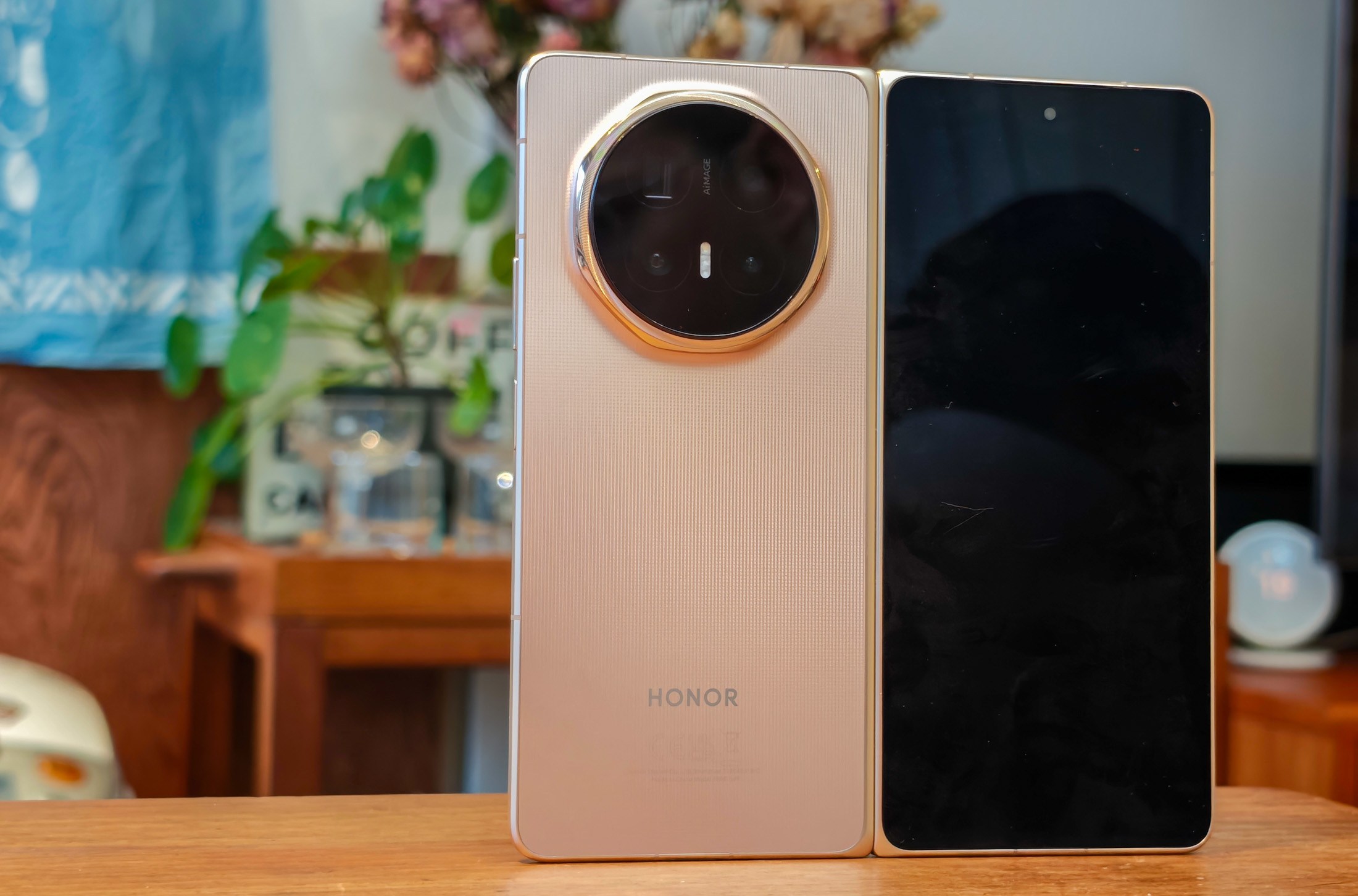 Photo of the Honor Magic V6, open, on a wooden table, showing the front screen and camera