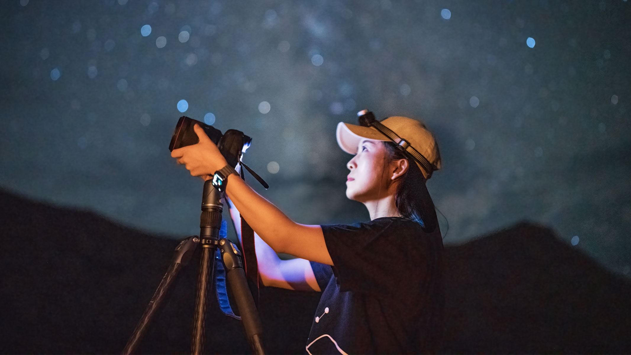 A woman using a camera with the night sky behind her.