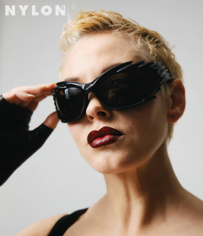 Woman with short blonde hair wearing black sunglasses and dark red lipstick, styled with edgy fashion for a bold look.