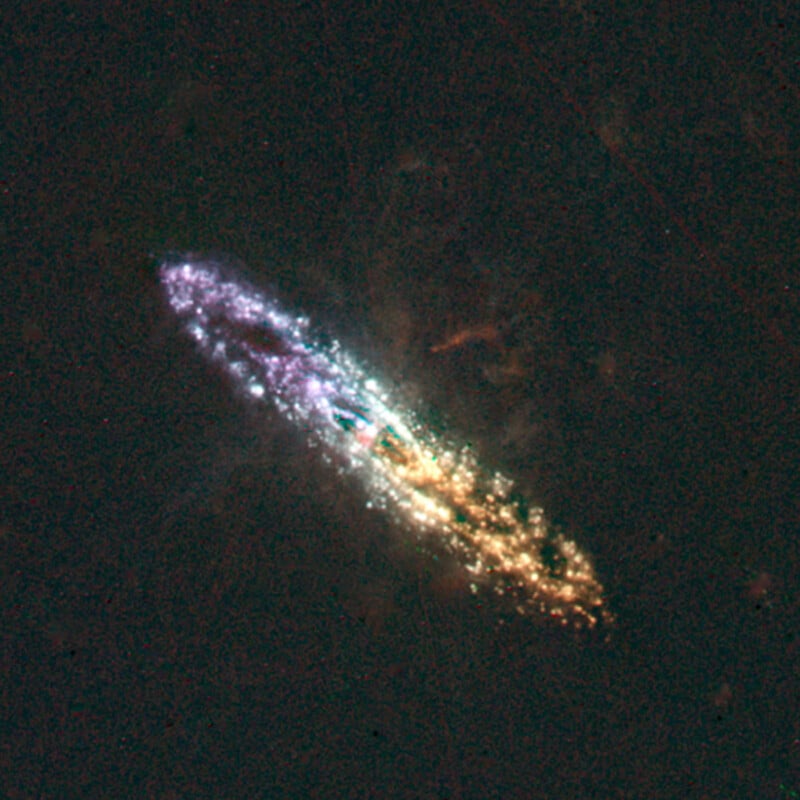 A colorful, elongated galaxy with sparkling clusters of stars in blue, purple, green, and orange hues, surrounded by the darkness of space.