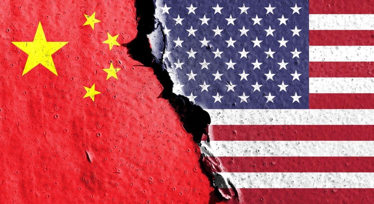 The national flags of the United States and China are split vertically down the middle by a prominent, jagged, dark crack. The left side displays the red flag of China with five yellow stars. The right side shows the American flag with its blue canton of white stars and red and white stripes. Both flags appear on a distressed, textured surface.
