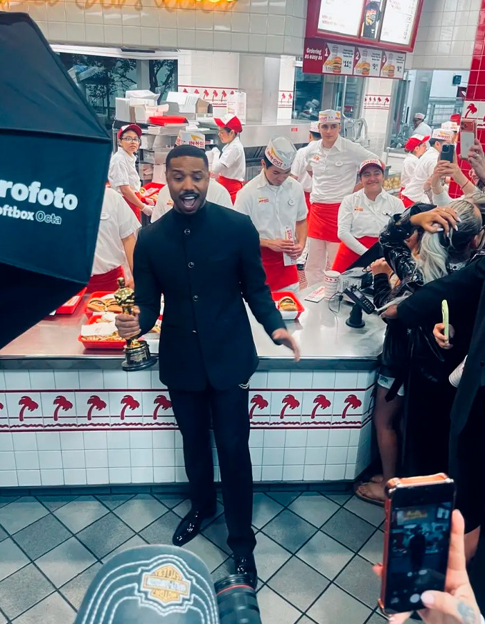 Michael B. Jordan holding Oscars trophy at fast food restaurant, attracting attention from staff and photographers.
