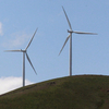 Seven modern windmills with three blades each stand along a hillside.