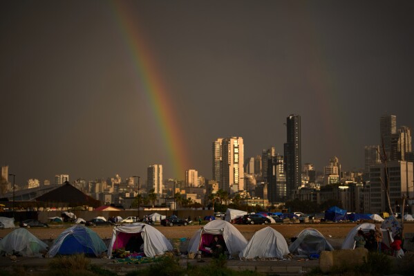 Displaced people who fled Israeli strikes in southern Lebanon sit inside tents used as shelters as a rainbow breaks through the rain in Beirut, Lebanon, Sunday, March 29, 2026. (AP Photo/Emilio Morenatti)