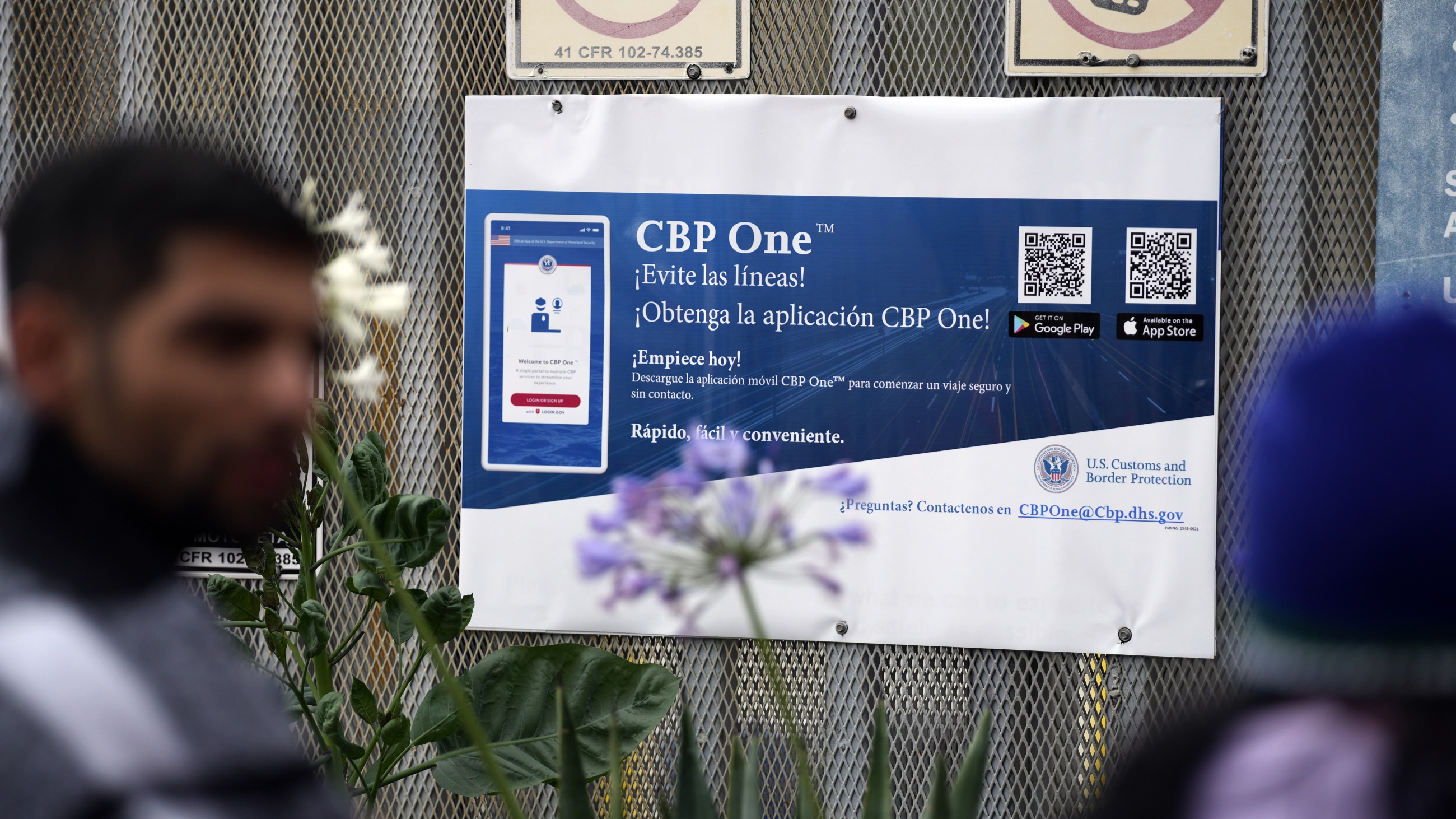 People waiting to apply for asylum stand in front of a sign for the CBP One app as they camp near the pedestrian entrance to the San Isidro Port of Entry, linking Tijuana, Mexico with San Diego.