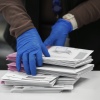A closeup shows the gloved hands of an election worker sorting mail-in ballots.