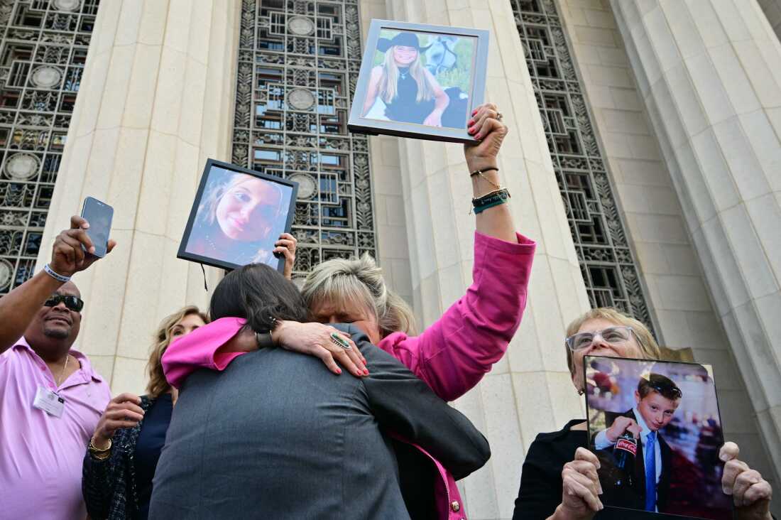 Relatives of victims hold up portraits of their loved ones, and two of them embrace, as they leave the courthouse.