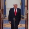 President Trump stands between two flags in the Cross Hall of the White House.