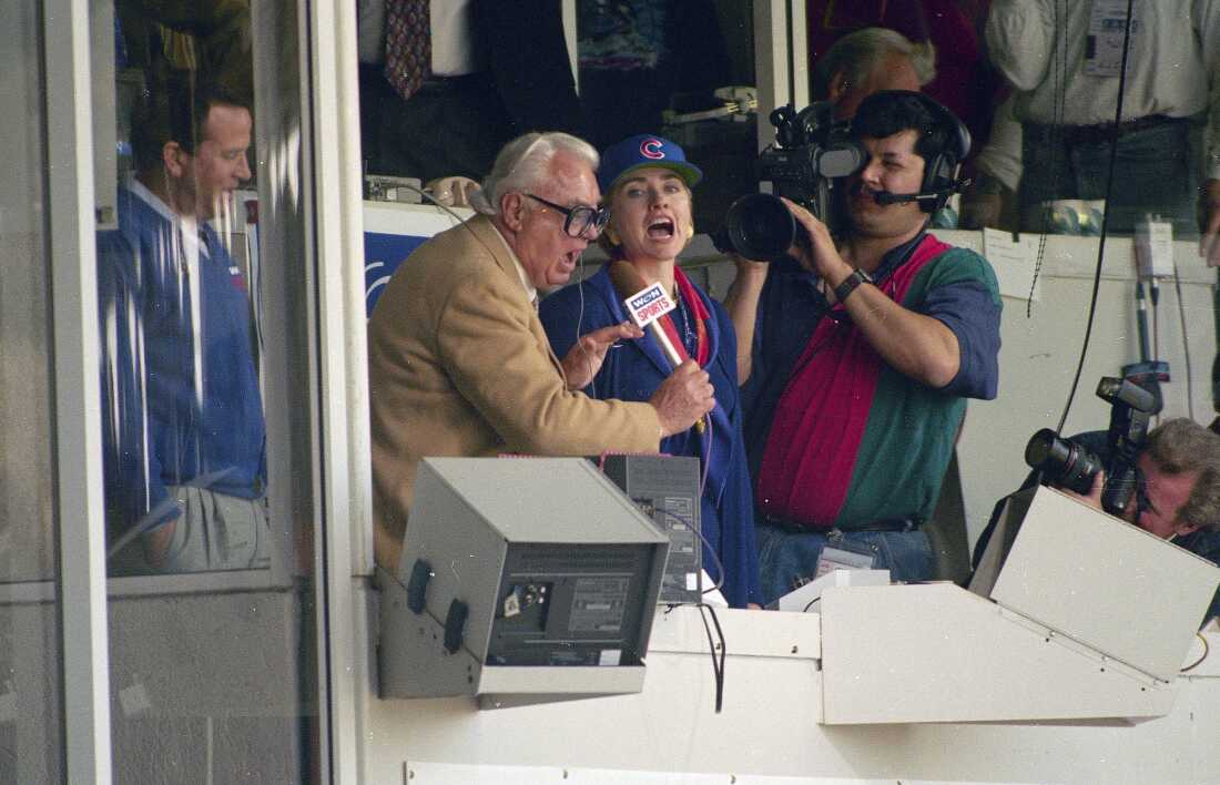 First lady Hillary Rodham Clinton, right, and Chicago Cubs announcer Harry Caray, left, sing "Take Me Out To The Ball Game" during the seventh inning stretch at Wrigley Field in Chicago in 1994. The Cubs are leaving WGN Radio that's been their radio home for 90 years. Radio president Jimmy de Castro confirmed on the air Wednesday, June 4, 2014, media reports that the Cubs are leaving the station after this season. (AP Photo/John Zich, File)