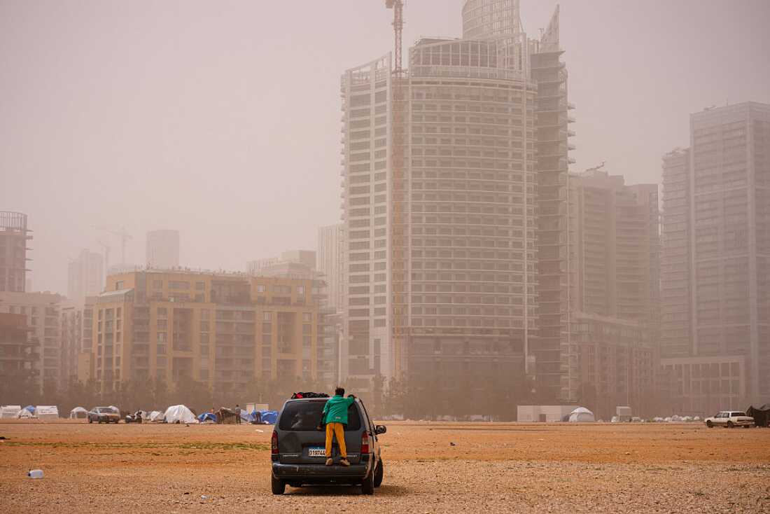 A displaced boy stands on the back of a car at an unofficial camp erected along Beirut's seafront area during a sandstorm on April 3, 2026.