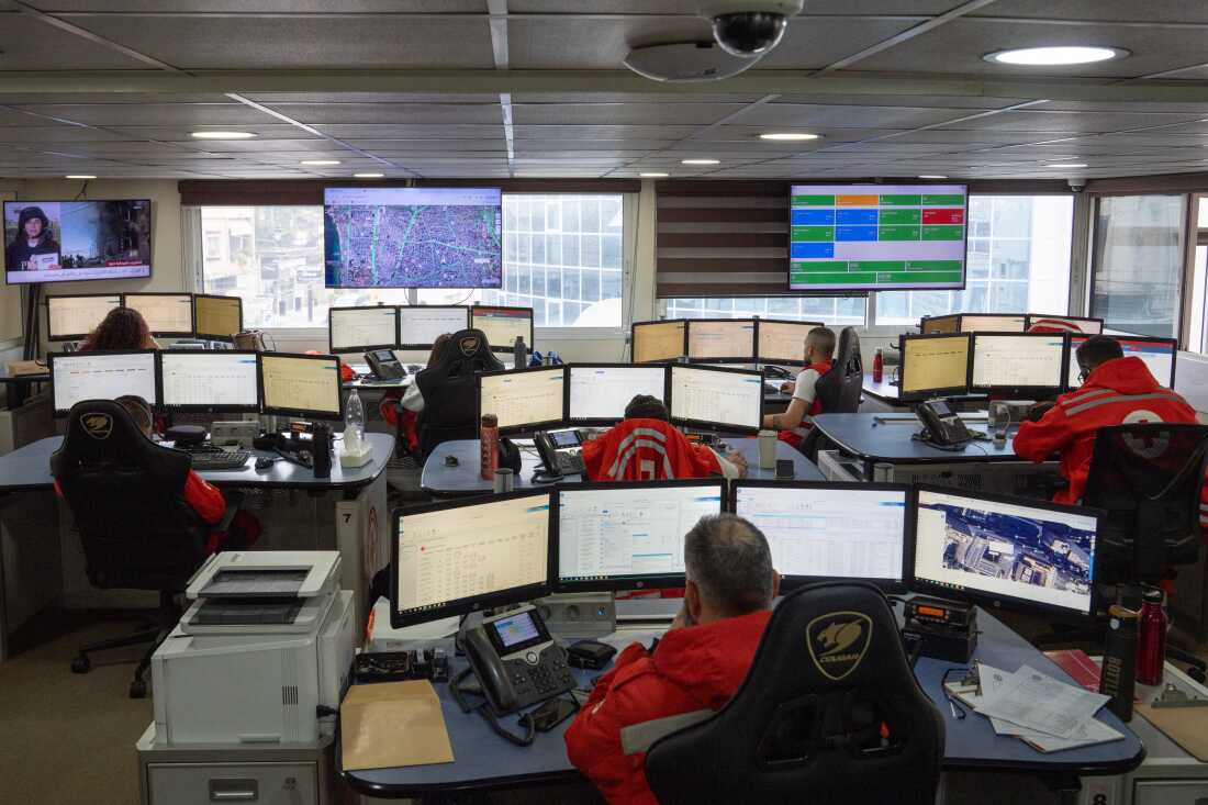 Eight people sit at desks with 3-4 monitors at the Red Cross dispatch center in southern Beirut.