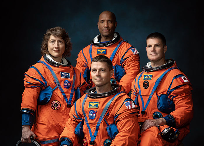 Four astronauts in bright orange NASA spacesuits posing against a dark background, highlighting NASA’s response to Travis Kelce’s tweet.
