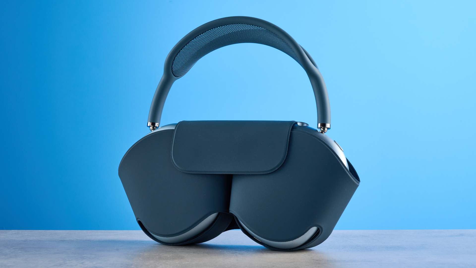 the apple airpods max 2 in blue photographed against a blue tom's guide background, showing the mesh headband, anodized aluminum ear cups, carry case, and controls