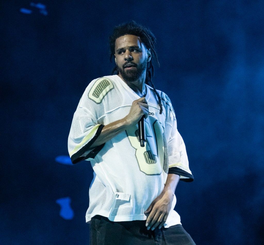 J. Cole performing on stage, wearing a white jersey.