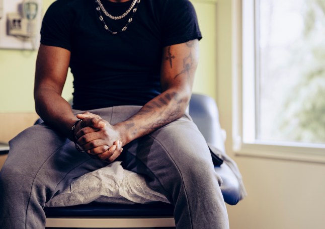 Midsection of man sitting on medical exam table with hands clasped