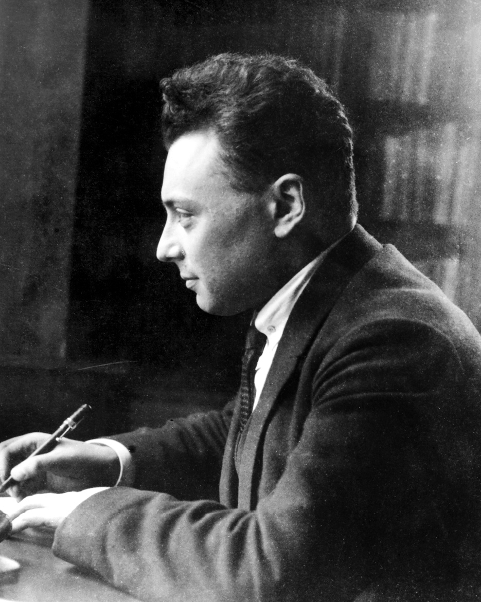 A man sits at a desk, holding a pen.