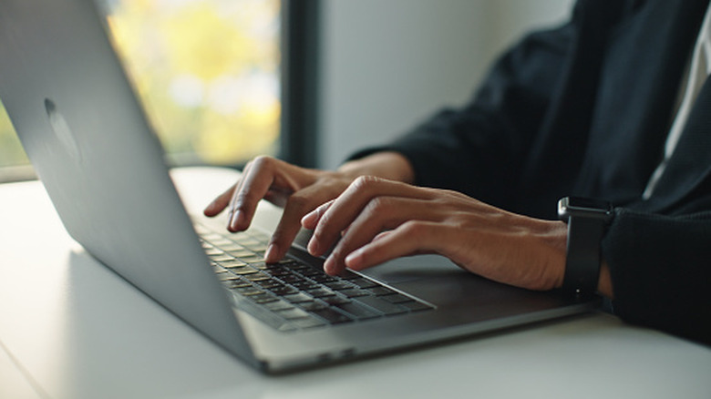 Person wearing a smartwatch typing on a laptop