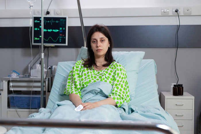 Young woman in hospital bed appearing distressed, connected to medical equipment monitoring vital signs.