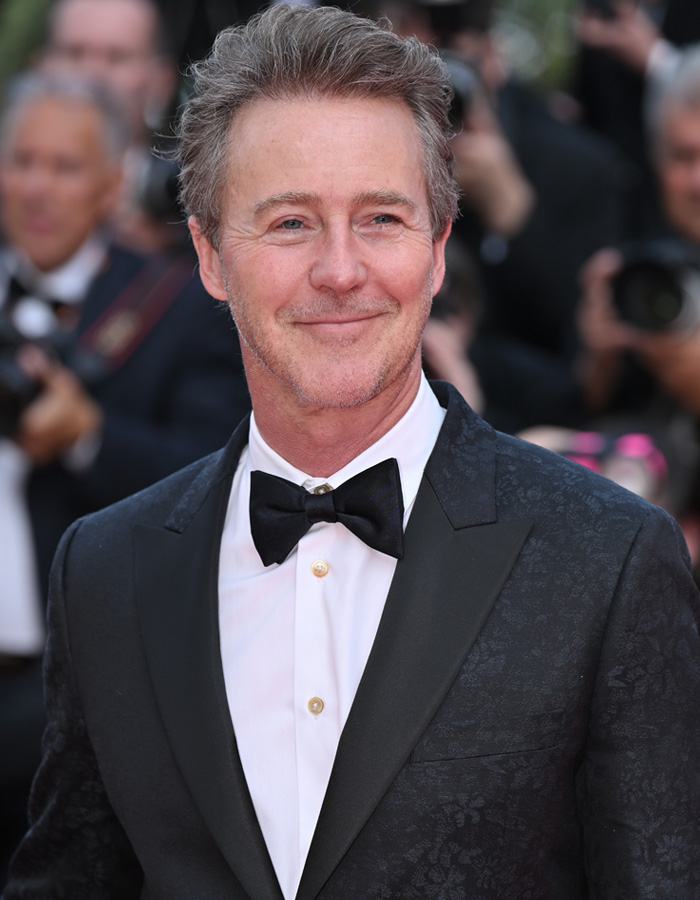 Brian C*x in a black tuxedo with bow tie at a red carpet event amid photographers capturing the moment.