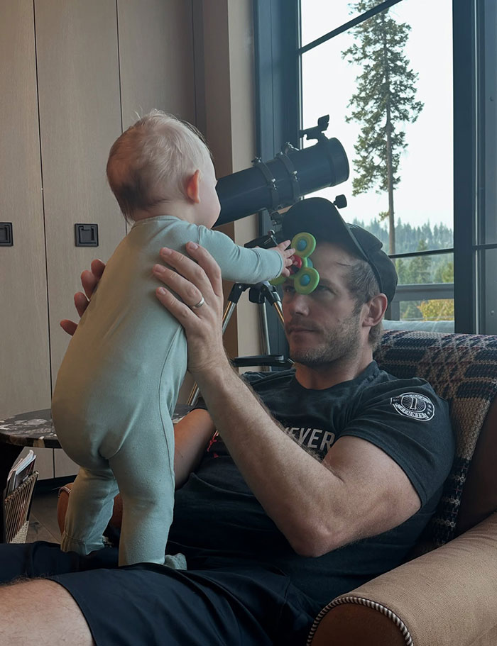 Chris Pratt holding baby in pajamas while the child plays with a fidget spinner in a cozy living room setting.