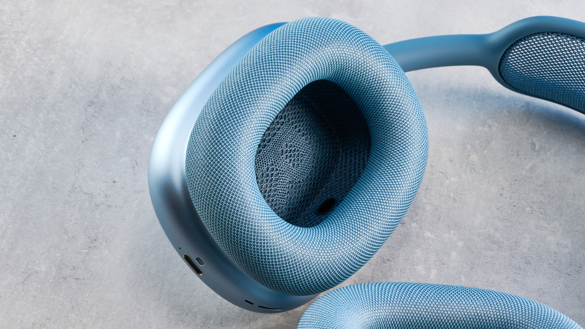 the apple airpods max 2 in blue photographed against a blue tom's guide background, showing the mesh headband, anodized aluminum ear cups, carry case, and controls