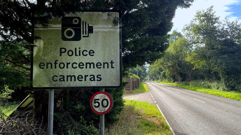 A police traffic enforcement camera located next to a speed limit sign on a rural road.
