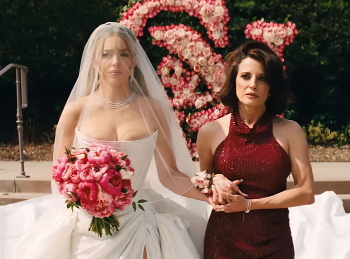 Sydney Sweeney in a white wedding dress holding a bouquet next to a woman in a dark red dress in Euphoria season scene.