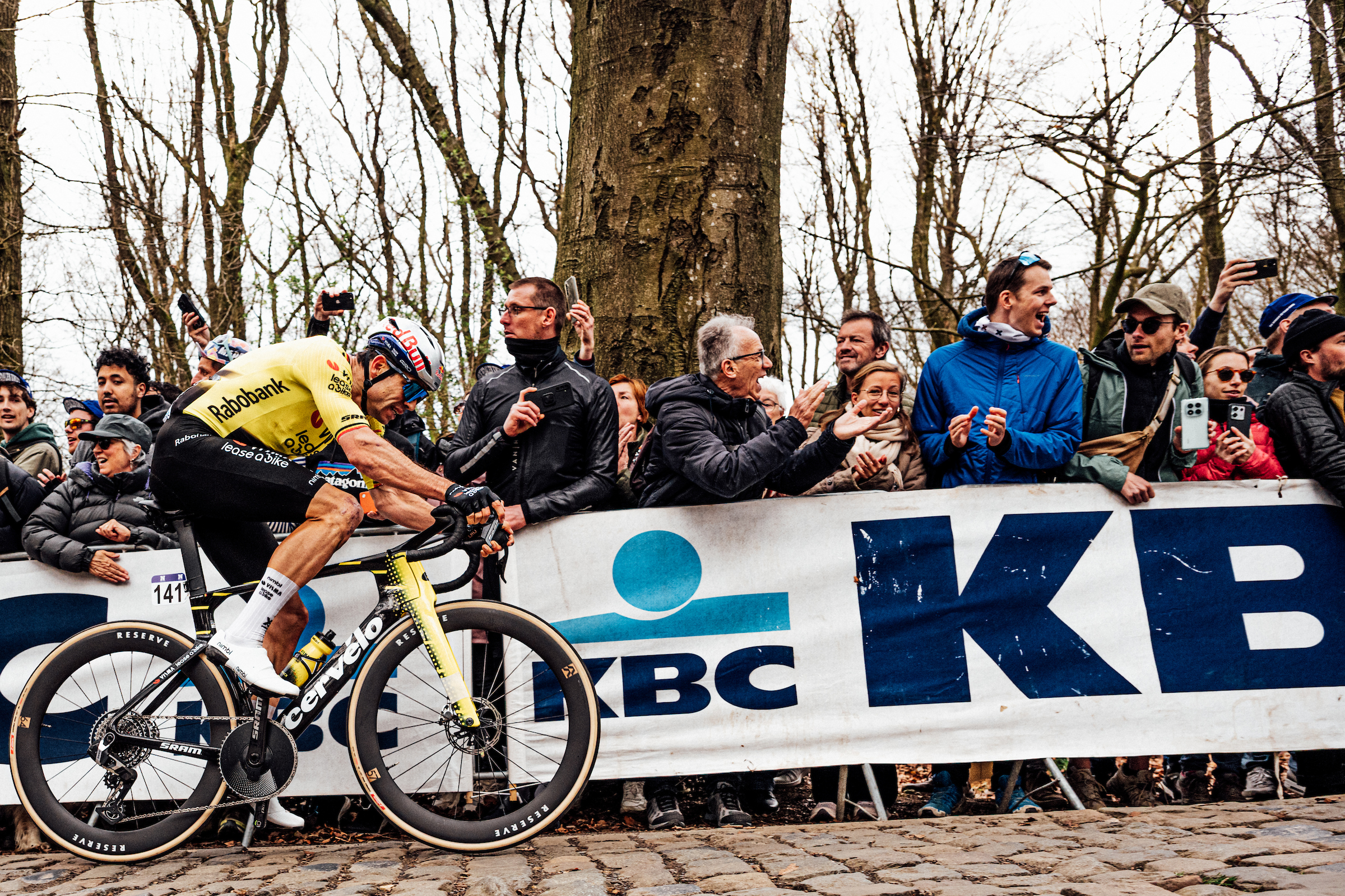 A side shot of Wout van Aert (Visma-Lease a Bike) riding up a cobbled climb during In Flanders Fields, with excited fans cheering behind a barrier