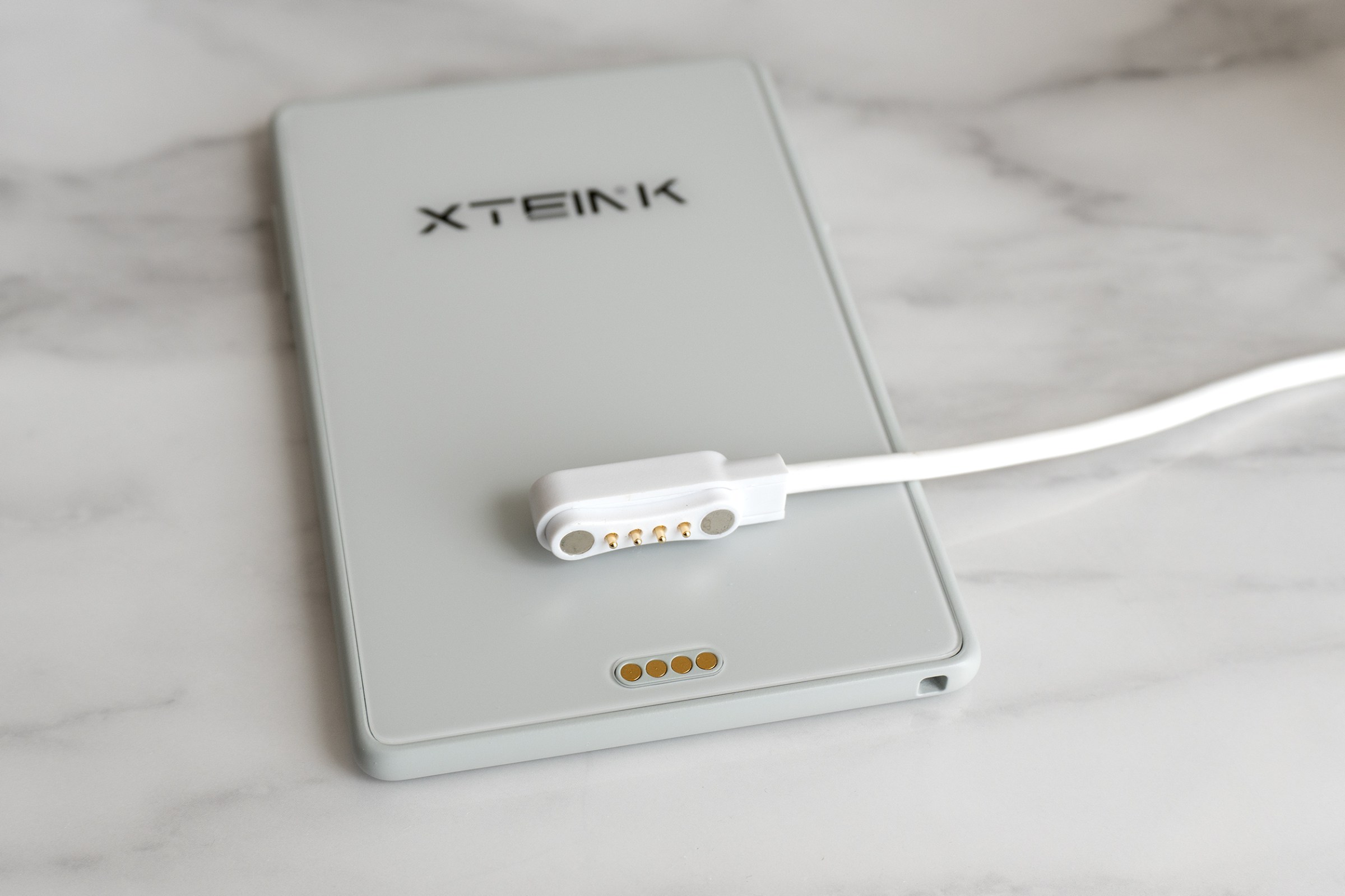 A proprietary charging cable laying on the back of the Xteink X3 e-reader.